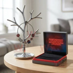 Silver adjustable charm bracelet with Stranger Things dice friends dont lie bicycle demogorgon flower and cassette charms hanging on a jewelry tree stand next to an open neon logo gift box.