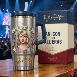 Stainless steel Taylor Swift themed tumbler with navy handle and straw next to a matching gift box on a wooden table with a concert stage and crowd in the background!