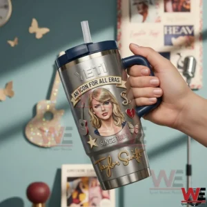 Person holding a stainless steel Taylor Swift themed tumbler with navy handle and straw in a decorated indoor room with posters and butterfly wall decor!