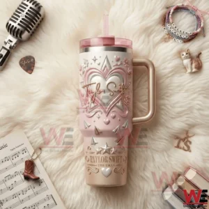 Pink and gold Taylor Swift themed insulated tumbler with straw and handle on a fluffy background surrounded by a microphone guitar pick sheet music bracelets and small decorative charms!