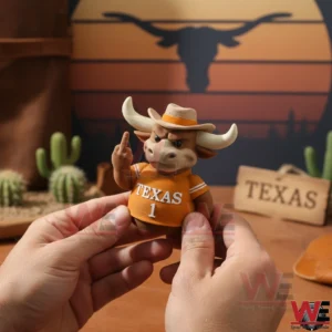 Hands holding a small angry bull figure with horns wearing a cowboy hat and an orange Texas number one shirt making a rude hand gesture in a western themed room with cacti and Texas decor.