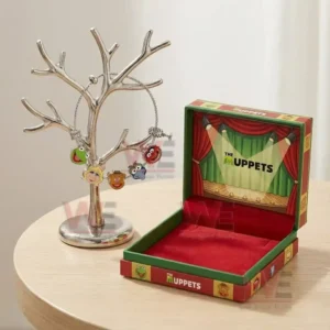 Adjustable charm bracelet on a jewelry tree stand with The Muppets character face charms next to an open red and green gift box on a wooden table.