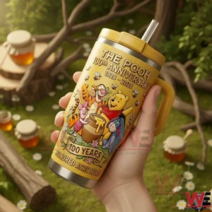 The Pooh 100th Anniversary 100 Years Hundred Acre Wood Tumbler 4 Hand holding a yellow The Pooh 100th Anniversary insulated tumbler with handle and straw featuring classic characters honey pot artwork and anniversary dates with a sunny garden background!