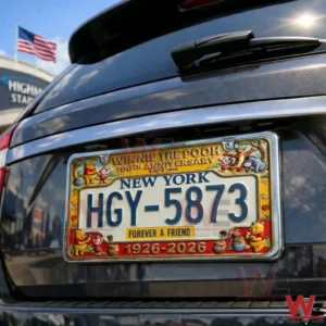 Rear of a dark car showing a New York license plate surrounded by a Winnie the Pooh anniversary themed decorative frame near a stadium!