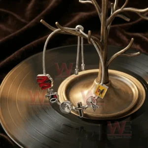 Silver adjustable charm bracelet with XO themed charms hanging on a jewelry tree stand above a vinyl record in a dark styled setting.