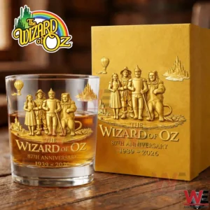 The Wizard of Oz 87th Anniversary 1939-2026 Gold Glass 3 A Wizard of Oz anniversary whiskey glass with amber liquid sits next to a gold presentation box showcasing detailed character engravings and commemorative design elements!