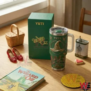 The Wizard of Oz Witch Hat Yeti Tumbler 4 Green Yeti tumbler with handle placed next to a Wizard of Oz themed box on a wooden table with props and a book!