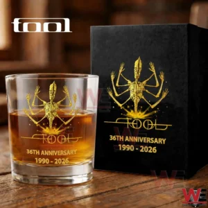 A commemorative TOOL whiskey glass with golden artwork and anniversary text placed next to a matching black collector box on a rustic table!