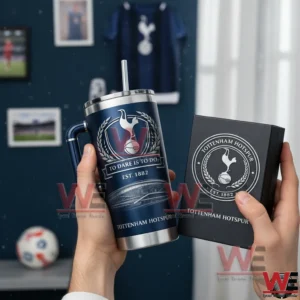 Tottenham Hotspur To Dare is To Do 1882-2026 Anniversary Tumbler Cup 3 Hands holding a navy Tottenham Hotspur insulated tumbler with handle and straw next to a collector style box in a club themed room with memorabilia behind!