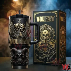 Black handled tumbler with embossed skull wings guitar and Volbeat lettering beside a matching themed gift box in a smoky stage setting!