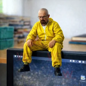 Bald man figurine wearing a yellow suit sitting on the top edge of a computer monitor with a blurred home office background!