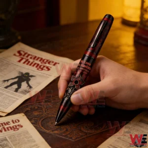 Hand holding a red and black Welcome To Hawkins tenth anniversary 2016 2026 pen next to Stranger Things themed papers on a wooden table!