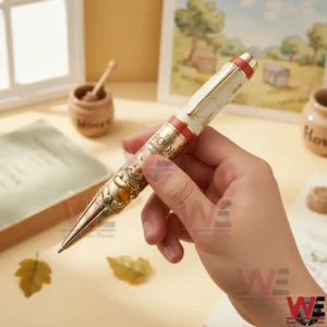 Hand holding a cream and gold Pooh anniversary pen with embossed Pooh artwork and honey themed details on a warm desk background!