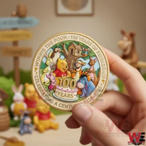 Winnie the Pooh 100th Anniversary 1926-2026 Coin 7 Hand holding a Winnie the Pooh one hundredth anniversary coin with Pooh and friends artwork while toys and themed decor appear softly blurred behind it.