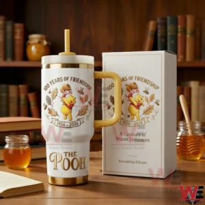 The Pooh 100 Years Of Friendship tumbler with handle and straw beside a matching gift box with gold accents honey jars and books in a cozy library background!