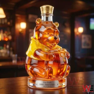 Honey colored bear shaped glass bottle with a gold cap and yellow shirt displayed on a wooden bar table with a warm bar background!