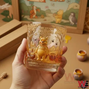 Winnie the Pooh 100th Anniversary Whisky Glass 3 Hand holding a Winnie the Pooh anniversary glass featuring detailed character art gentle honey tones and a charming storybook background!