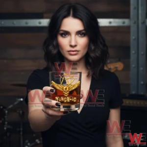 A woman in a black outfit presents a Yungblud whiskey glass forward showing a detailed gold skull with wings and the Yungblud name in sharp focus!