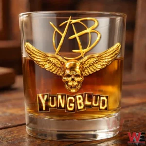YUNGBLUD I Was Made for Lovin you Gold Glass 11 A Yungblud whiskey glass sits on a wooden table with amber whiskey inside highlighting the gold skull wing emblem and prominent Yungblud branding!