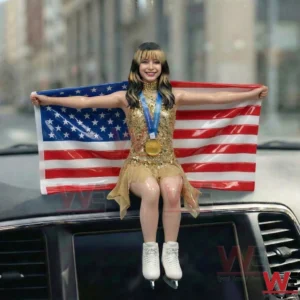 Mini figure skater in a gold dress holding a United States flag and wearing a medal on a car dashboard!