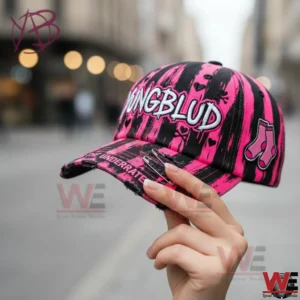 Hand holding pink and black Yungblud baseball cap with embroidered logo and distressed brim.