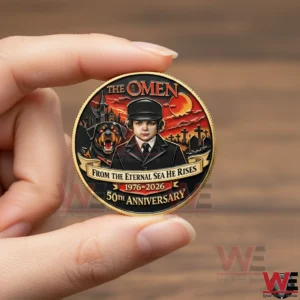 Hand holding The Omen 50th Anniversary coin showing boy and Rottweiler design.