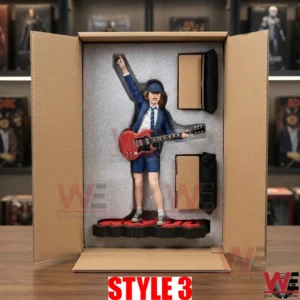 A high quality photograph shows an open cardboard box with a custom grey foam insert holding a detailed collectible figure of Angus Young from AC DC in his schoolboy uniform with a red SG guitar! The figure is posed dynamically with one arm up! The base and separate components are nestled in form fitting cutouts in the foam! The box sits on a wooden desk with blurry background shelves full of collectibles and music records!