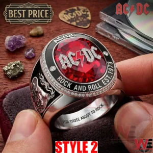 Close up of a hand holding an AC DC ring with a red gem and diamond accents over a wooden background with music accessories!
