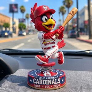 A photo of a Fredbird mascot bobblehead figure on the textured dashboard of a vehicle! The figure is spring mounted and faces away towards the street visible through the windshield! The base has the text CARDINALS EST 1882!