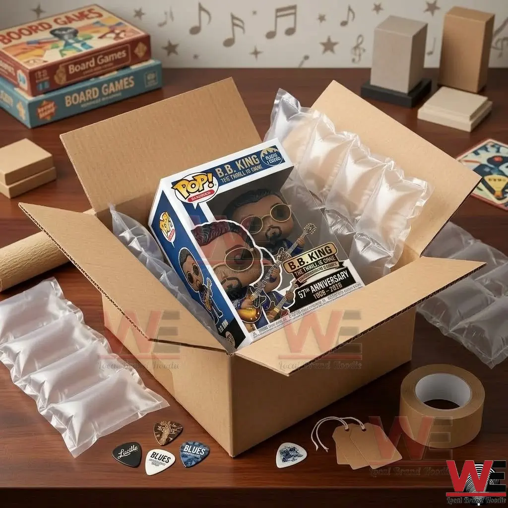 BB King Guitar The Thrill Is Gone Pop Figure Doll 2 An overhead photograph looking inside an open cardboard box! The B.B. King vinyl figure and its collector packaging are clearly visible within the box, surrounded by protective air pillow void fill! The wooden desk surface below holds shipping tape, tags, loose picks, and other boxes!
