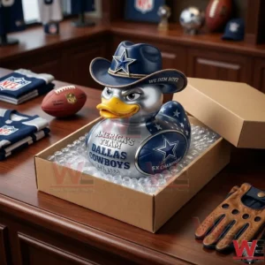 Dallas Cowboys Americas Team 5x Champions Duck 3 The silver Dallas Cowboys rubber duck is packaged inside a cardboard box with bubble wrap on a wooden desk. Team jerseys and a football are visible on the table surface next to the box.