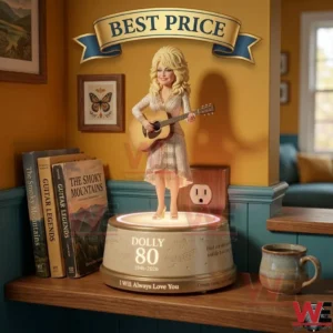 A blonde female singer figurine playing a guitar on a light up base! The base is labeled Dolly 80! It is placed on a wooden shelf next to a stack of books and a coffee cup! A blue and gold banner is displayed above the figure!