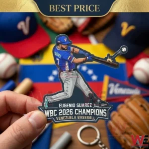 A hand holds a celebratory Eugenio Suarez sticker showing him hitting a baseball. The sticker mentions the WBC 2026 Championship and Venezuela Baseball. The background includes various baseball equipment and a Venezuelan flag.