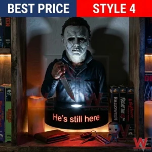 A Michael Myers bust holding a knife on a glowing base that says HE IS STILL HERE! The scene is dark with VHS tapes and a wallet on the shelf!