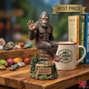 A waving Bigfoot figure on a spring base displayed on a wooden table alongside a coffee mug and books!