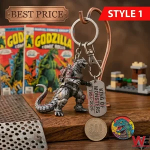 A silver Mechagodzilla keychain hanging on a metal stand with a tag that says KING OF MONSTERS! There are comic books and a monster pin on a wooden table!