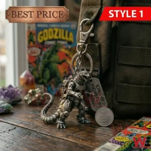A silver Mechagodzilla keychain clipped to a green bag! A metal tag and a silver coin are visible against a wooden background with crystals and a comic book!