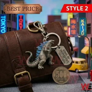 A Godzilla keychain with blue fins hanging from a brown leather bag! A metal tag and a gold coin are on the ground in a miniature city setting!
