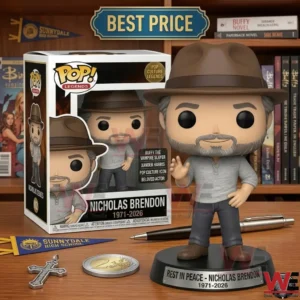 A vinyl figure of an actor with a beard and brown hat on a memorial base! The figure stands next to its white collector box on a wooden desk! Items like a cross necklace a coin a pen and school pennants are arranged around it! The background shows a shelf of books and media!
