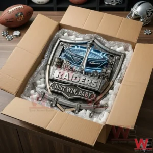 Raiders Just Win Baby Wall-Mounted Key Holder 5 An open cardboard box containing a Raiders metal wall rack! The item is protected by bubble wrap and foam peanuts! The plaque features a glowing stadium and metallic lettering! The box sits on a wooden surface with sports gear nearby!