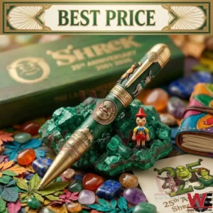 Commemorative Shrek 25th anniversary pen with gold accents and character reliefs lying on green stone and scattered colorful gems.