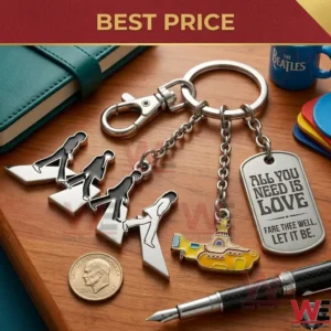 A top down photograph of a Beatles themed multi charm metal keychain on a wood grain desk! The three charms are the band silhouettes walking a Yellow Submarine and an engraved metal tag! A green notebook a blue mug a coin and a pen are positioned around the keychain on the desk!
