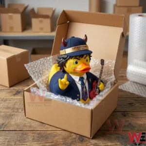 A rubber duck figure of Angus Young with horns inside a cardboard box! It is surrounded by packaging materials!
