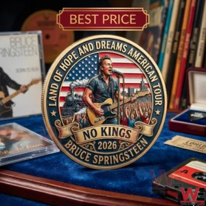 Close up view of a circular Bruce Springsteen commemorative coin with a detailed central scene of a performance and a surrounding text border! It sits on a blue velvet cloth amongst records tapes and other rock memorabilia in a slightly blurred background!