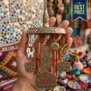 A detailed metal wind chime with Coca Cola branding and anniversary plaques held against a blurry colorful background!