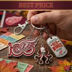 A three part metal keychain for the Detroit Red Wings is held over a desk! It features a one hundredth anniversary logo an octopus charm and a dog tag with team details!