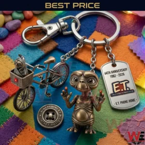 A close up photograph of an ET movie anniversary keychain! It includes charms of a bicycle with ET in a basket a standing ET figure and an engraved metal tag! The items are placed on a bright multicolored patchwork fabric!