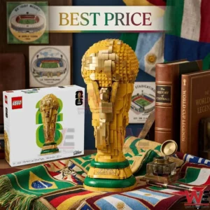 A gold Lego trophy based on the World Cup design stands next to its packaging on a wooden surface with soccer themed decorations.