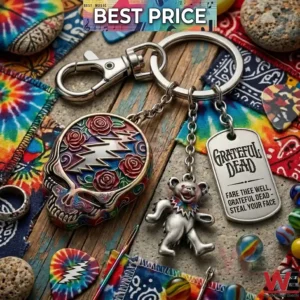 A close up photograph of a Grateful Dead themed keychain with a skull charm a dancing bear and an engraved tag! The items are surrounded by tie dye fabric guitar picks and marbles on a wooden surface!