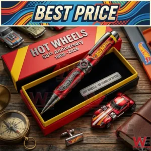 A top-down angled shot of a limited edition Hot Wheels 58th Anniversary pen set in an open presentation box. The pen is red, metallic, and detailed with logos. Surrounding it on a wooden table are several collectible die cast cars, a compass, cuff links, and track pieces. A graphic banner is at the very top.